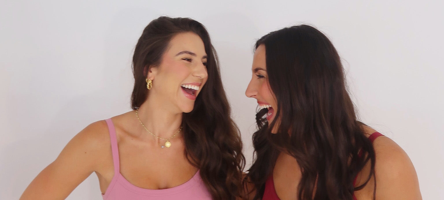 Two women laughing together against a plain background
