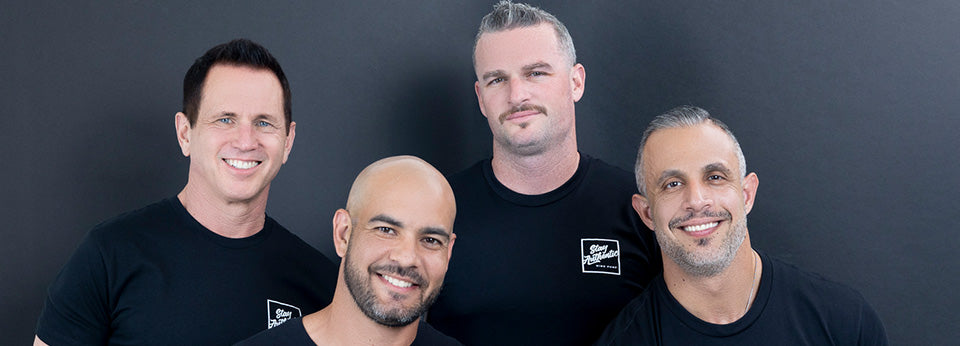 Four men posing together against a dark background