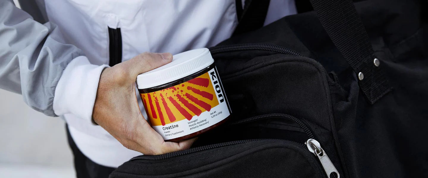 A person in a white jacket holds a white jar with a red and orange sunburst label next to a black duffel bag.