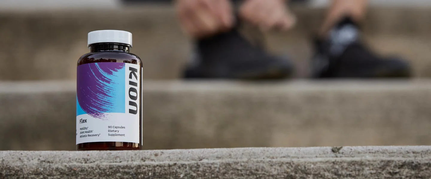 A bottle of Kion Flex capsules standing on a concrete ledge, with a blurred person's legs and shoes in the background on outdoor steps.