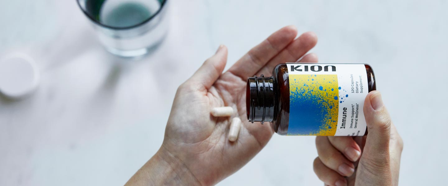 Person holding a bottle of Kion supplements with a glass of water on a light surface.