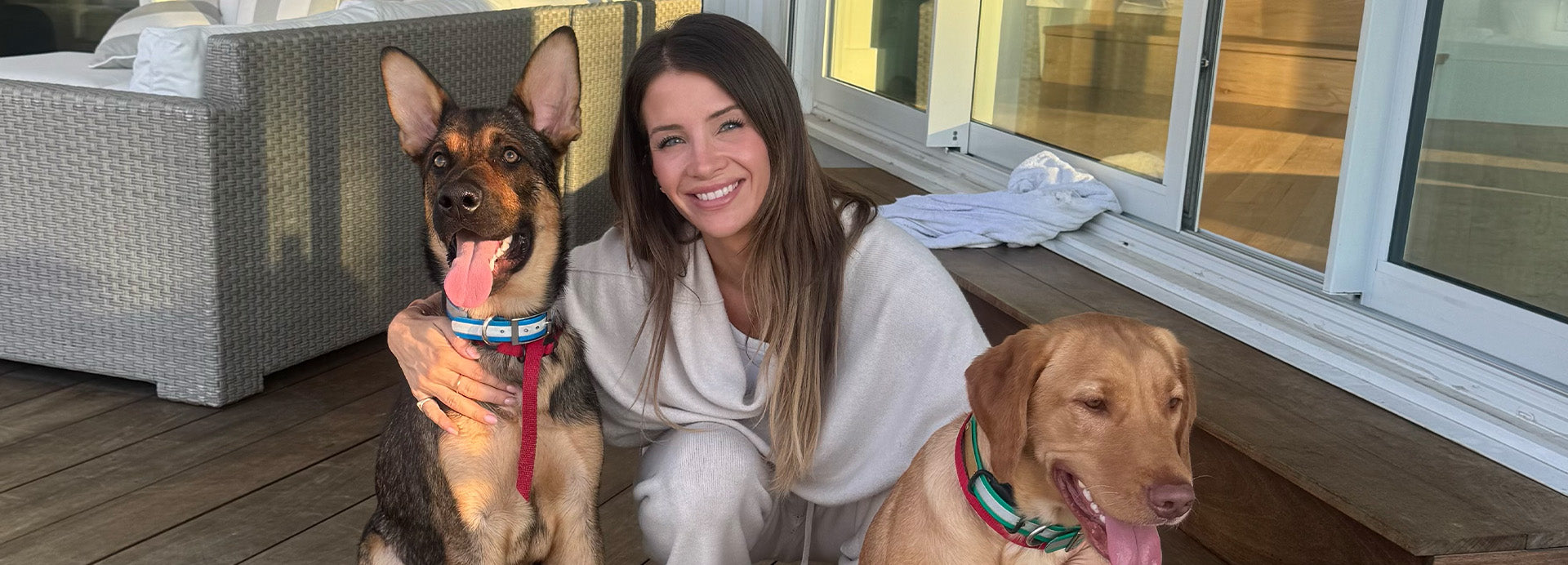 Woman sitting on a deck with two dogs, smiling at the camera.
